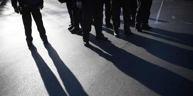 Polizistinnen und Polizisten stehen in der Abenndsonne auf einer Straße, zu erkennen sind nur ihre Beine und der Schatten, den sie werfen.