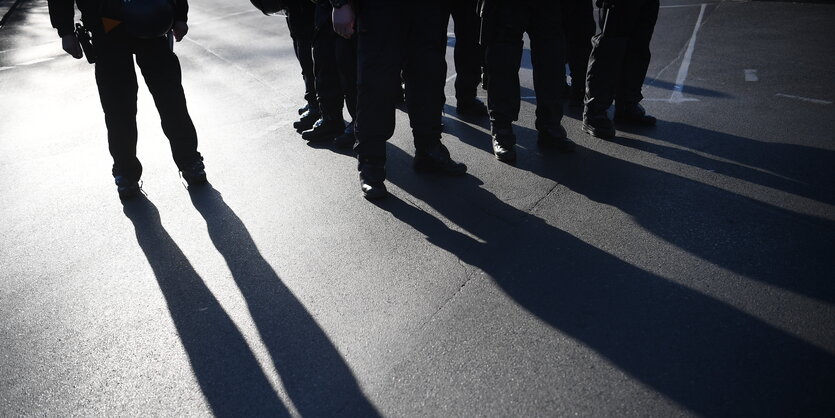 Polizistinnen und Polizisten stehen in der Abenndsonne auf einer Straße, zu erkennen sind nur ihre Beine und der Schatten, den sie werfen.