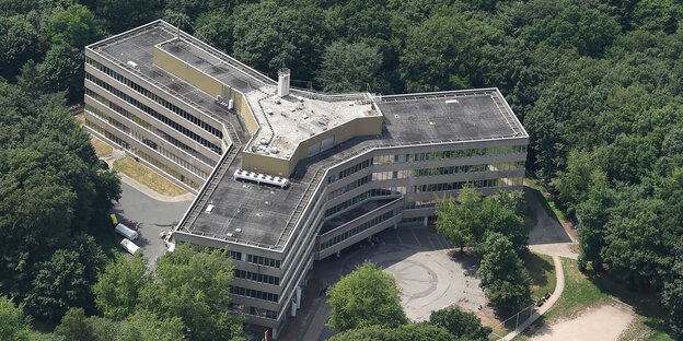Eine Luftaufnahme zeigt ein mehrstöckiges Gebäude mit drei Seitenflügeln umringt von Bäumen