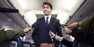 Justin Trudeau steht in einem Flugzeug, viele Mikrofone sind auf ihn gerichtet