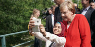 Ein Mädchen hält ihr Smartphone hoch, hinter ihr steht Angela Merkel