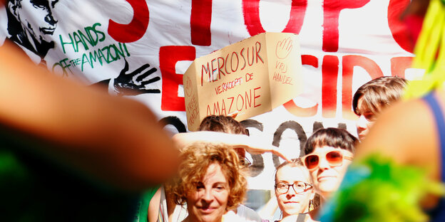 Demonstrantinnen stehen vor einem Plakat, auf dem "Stopp Mercosur" und der brasilianische Präsident Bolsonaro zu sehen sind