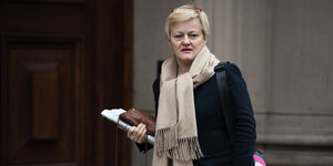 Die Grünen-Politikerin Renate Künast steht vor einer braunen Holztür, in der Hand hält sie eine Zeitung sowie eine Handtasche.