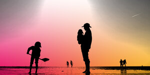 EIn Mann mit Sonnenhut steht am Strand, auf dem Arm trägt er ein kleines Kind. Vor ihm schippt ein Junge Sand. Die Sonne scheint und taucht alles in gelbes Licht. Die Menschen sind nur an ihren schwarzen Umrissen zu erkennen.