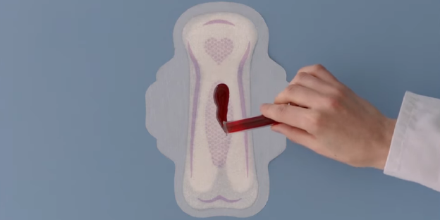 Aus einem Reagenzglas wird Blut auf eine Binde geträufelt.