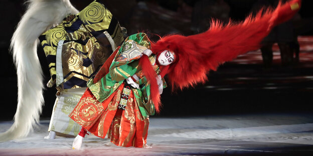 Eröffnungszeremonie bei der Rugby WM in Tokio. Zwei Menschen sind als Kabuki kostümiert. Sie tragen bunte kleidung und lange Haare, die durch die Luft fliegen