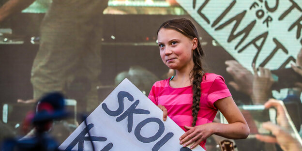 Greta Thunberg steht auf eine Bühne mit einem Transparent in den Händen