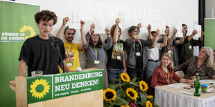 obert Funke (l, Bündnis 90/Die Grünen), Sprecher der Grünen Jugend Brandenburg, spricht auf dem kleinen Parteitag der Grünen in Brandenburg, während andere Mitglieder der Grünen Jugend Schilder mit Buchstaben hochhalten, die die Aufschrift "#Keenja" ergeb