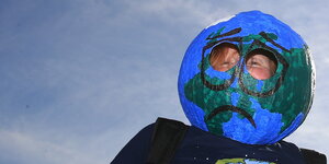ein Mensch trägt einen Pappmaschee-Globus mit einem aufgemalten traurigen Gesicht um den Kopf