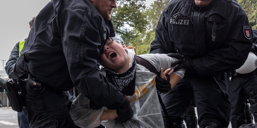 eine schreiende Frau wird von zwei Polizisten weggeschleppt