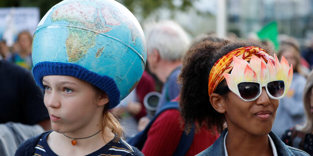 Ein Junge und ein Mädchen, mit Feuermaske und Erdball-Atrappe auf dem Kopf demonstrieren gegen die lasche Klimapolitik