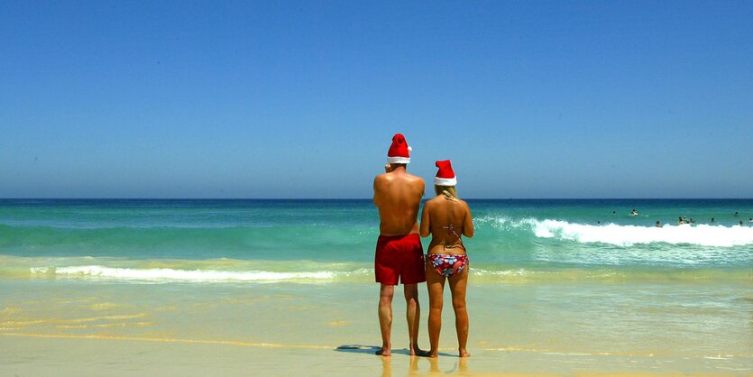 Ein Pärchen mit Weihnachtsmützen in Badesachen am Strand