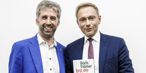 Boris Palmer und Christian Linder stehen nebeneinander und lächeln. Lindnert hält ein Buch hoch