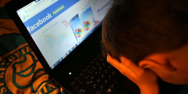 Junge sitzt mit Händen am Kopf vor einem Laptop: Darauf ist Facebook geöffnet