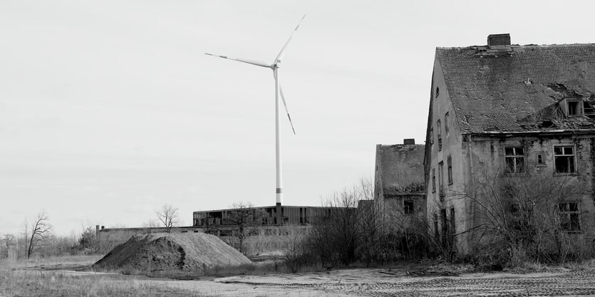 Man sieht auf dem schwarzweißen Bild ein Windrand hinter verlassenen Häusern mit leeren Fensterhöhlen