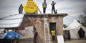 Männer stehen in der Nähe und auf einer Hütte, auf dem Dach steht ein Schild mit der Aufschrift "Water is not for drink"