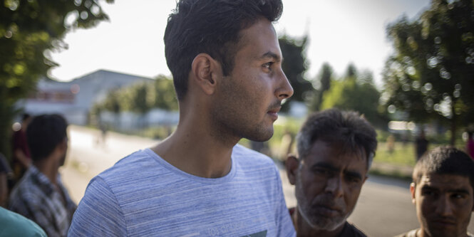 Ein junger Mann in weißem Shirt ist umringt von anderen jungen Männern, fotografiert im Profil