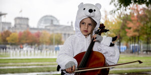 Ein Mädchen im Eisbärenkostüm spielt Cello. Im Hintergrund ist das Reichstagsgebäude zu erkennen.