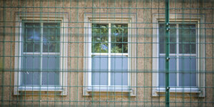 eine Hausfassade mit abgeklebten Fenstern hinter einem Gitterzaun