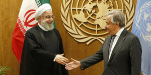 Hassan Rouhani schüttelt Antonio Guterres die Hand. Im Hintergrund das Emblem der UN