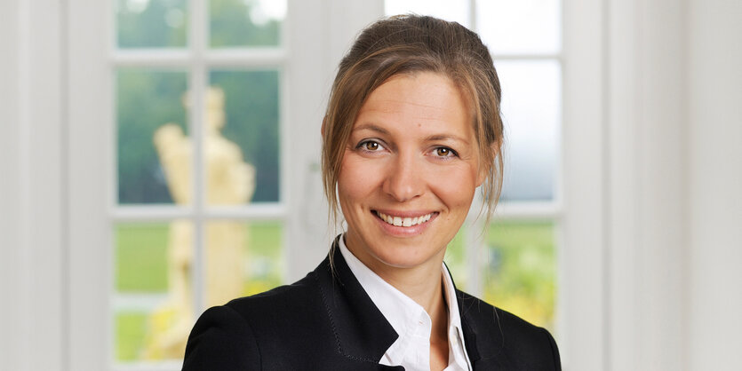 Brustbild Susanne Menzel-Riedls vor einem weißen Fenster.