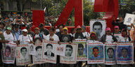 Angehörige und Mitbürger demonstrieren in Mexiko-Stadt. Sie halten Schilder mit Bildern ihrer vermissten Söhne in den Händen. Im Hintergrund steht eine große rote 43.