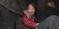 Ein etwa vier Jahre altes Kind in rotem Mantel steht zwischen Frauen in schwarzen Umhängen. Ihre Köpfe sind sind nicht zu sehen. Das Kind weint.