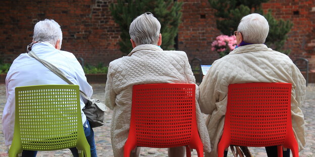 drei Rentnerinnen, die auf Plastikstühlen sitzen, von hinten