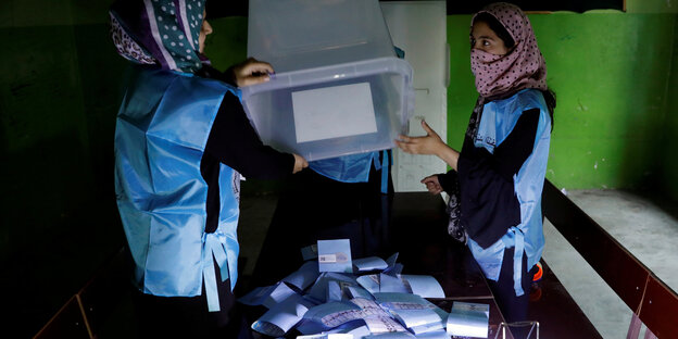 zwei Frauen leeren den Inhalt einer Wahlurne auf einen Tisch