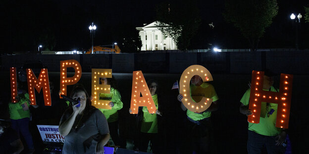 Menschen halten im Dunkeln die Buchstaben des Wortes Impeach in die Luft.