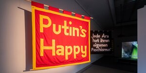 auf einem hängenden Stück Stoff steht „Putin's happy“, daneben hängt ein weiteres Stück Stoff, auf dem steht „Jede Ära hat ihren eigenen Faschismus“