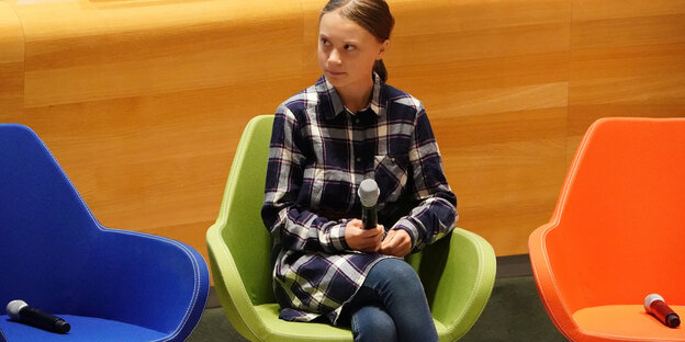 Greta Thunberg sitzt mit Mikrofon auf einem Stuhl, die beiden Stühle neben ihr sind noch frei