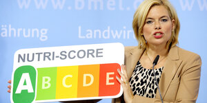 Julia Klöckner steht bei einer Pressekonferenz vor einer blauen Fotowand und hält die Ernährungsampel Nutri-Score in den Händen.