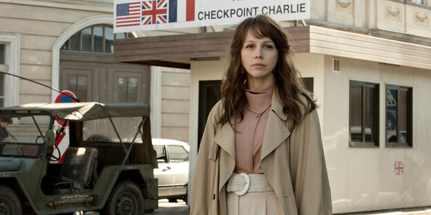Eine Frau in einem Mantel steht vor einem historischen Nachbau des Checkpoint Charlie