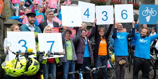 Leute in Fahrradkleidung halten Schilder mit Zahlen hoch