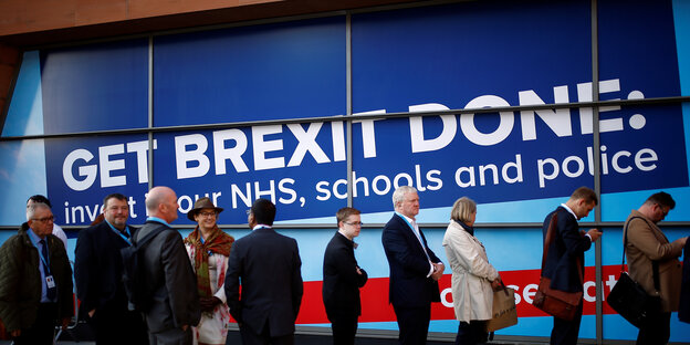 Wartende Parteitagsdelegierte vor einem großen blauen Plakat auf dem steht: Get Brexit Done
