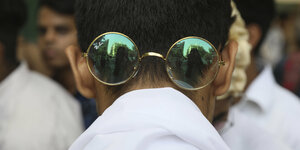 Ein Mann trägt die ikonisch-runde Brille von Gandhi auf dem Hinterkopf.