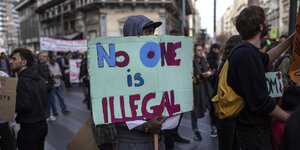 Ein Mann hält ein Schild aus Pappe, darauf steht: "No one is illegal."