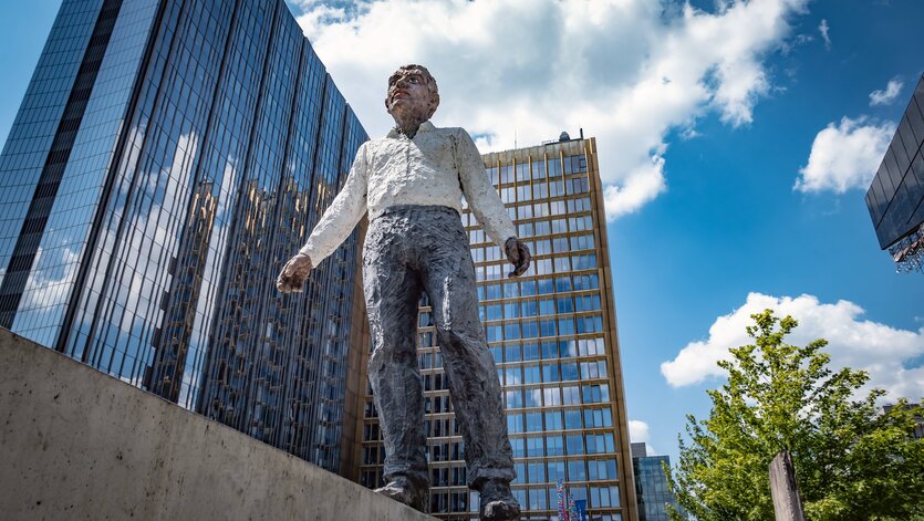 Skulptur eines balancierenden Mannes vor einem Hochhaus