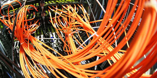 Zahlreiche orangefarbene Glasfaserkabel führen auf die Schalttafel eines Computers