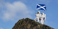 Gestaltenin Raumfahreranzügen halten eine schottische Fahne