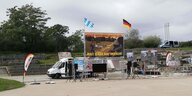 Ein weisser Lieferwagen steht im Görlitzer Park. Davor sind Plakate und Schilder mit den Parolen der Pegida aufgebaut. Über allem wehen eine Bayern und eine Deutschland Flagge.