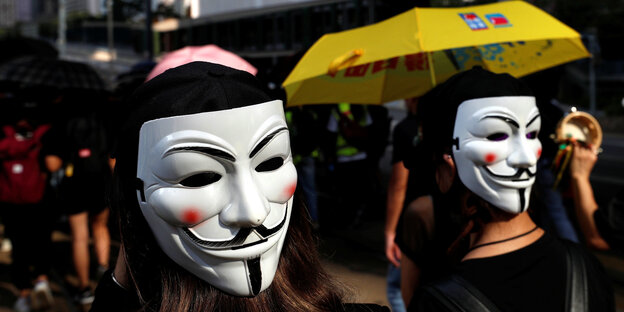 Zwei Protestierende mit Masken auf dem Hinterkopf und einem gelben Regenschirm