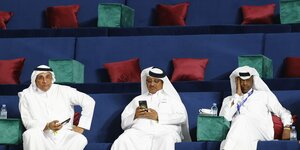 Drei Scheiche sitzen auf der Zuschauertribühne der Leichtathletik-WM in Doha und gucken gelangweilt auf ihr Smartphone