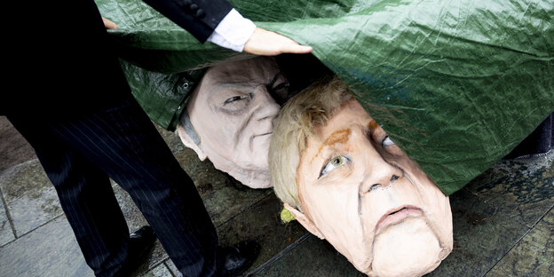 Masken von Merkel und Scholz unter einer grünen Plastikplane