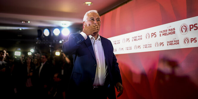 Der sozialistische Kandidat neben einer roten Wand, im Hintergrund Fotografen. Er hält sich die Hand vor den Mund