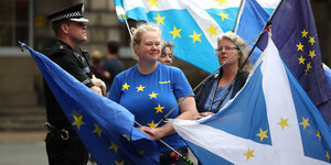 Zwei Frauen schwingen EU-Fahnen und tragen EU-Shirts, daneben ein Polizeibeamter