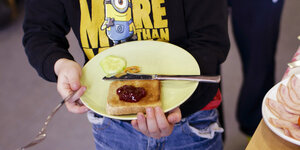 Ein Kind hält einen Teller in der Hand, auf dem ein Marmeladenbrot liegt