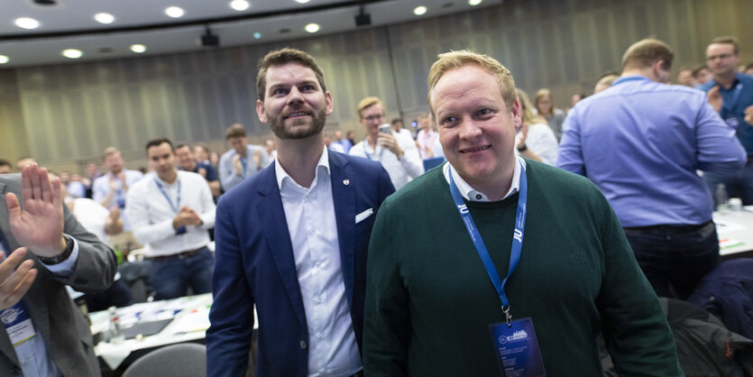 Zwei junge Männer laufen durch einen Saal, sie bekommen Beifall von links und rechts