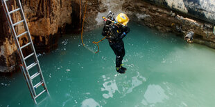 Ein Taucher springt in eine mit Wasser gefüllte Baugrube einer Großbaustelle